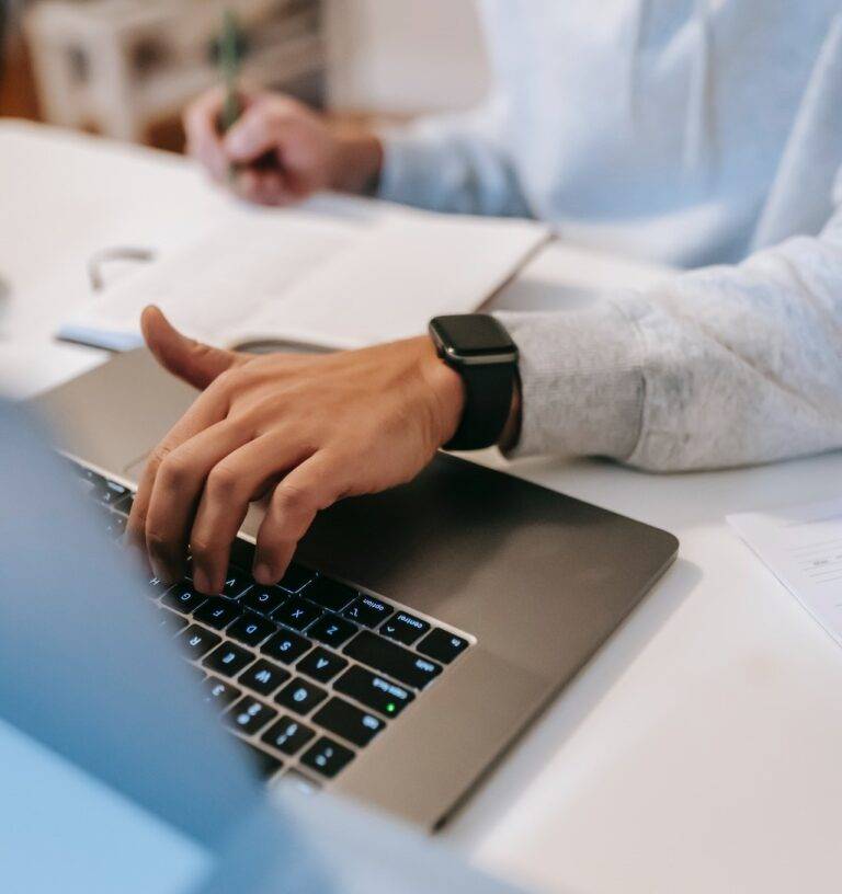 Person Typing on a laptop's keyboard while taking notes with the other hand