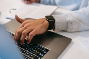 Person Typing on a laptop's keyboard while taking notes with the other hand